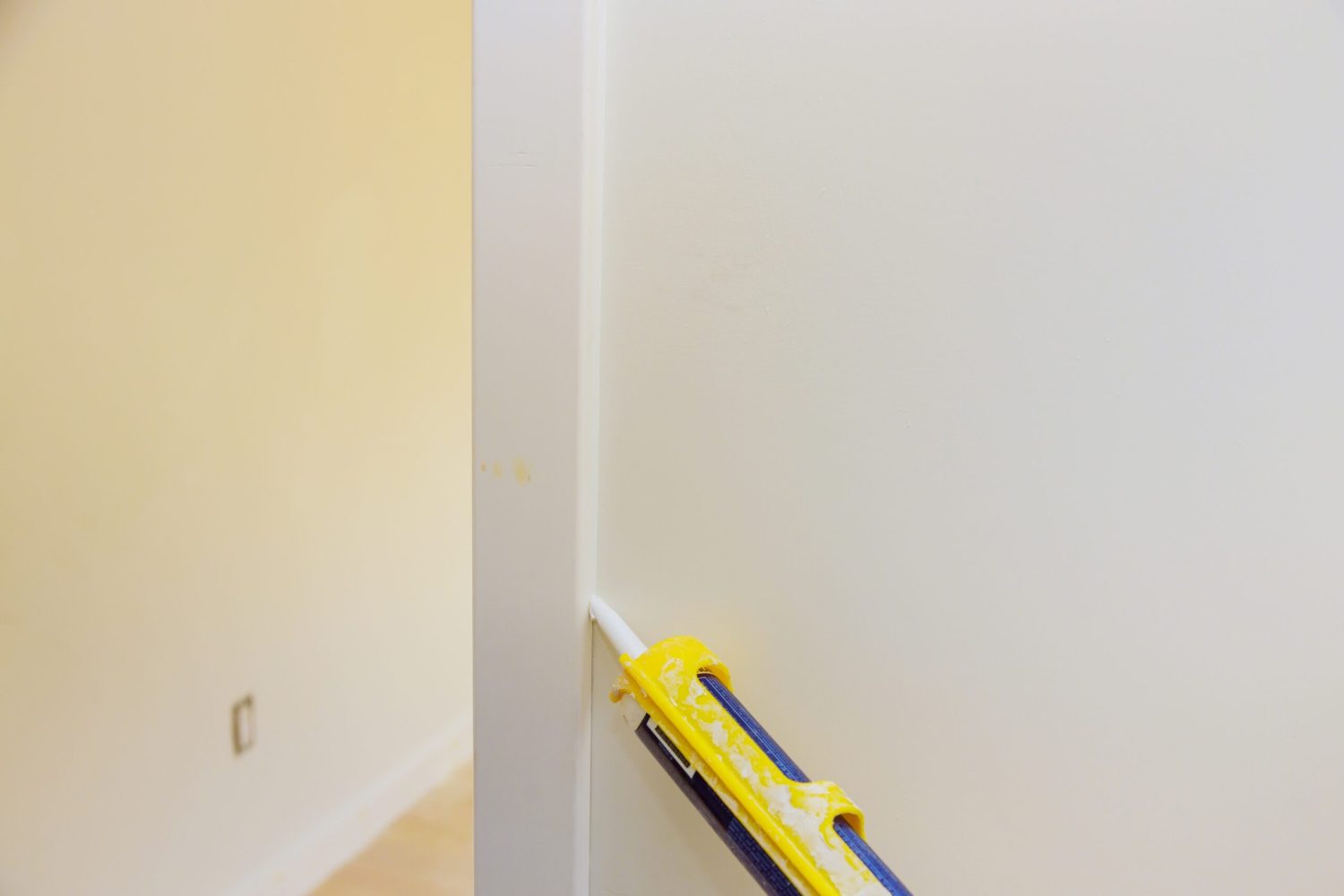 Worker hands applying silicone sealant with caulking gun for repairing door molding trim